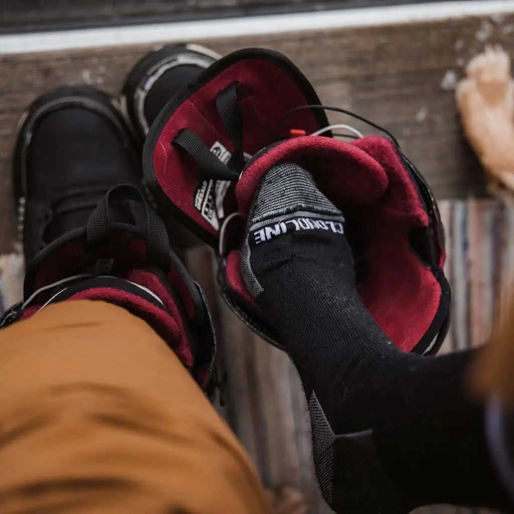 Snowboarder wearing Black Cloudline merino wool snowboard socks putting on snowboard boots.