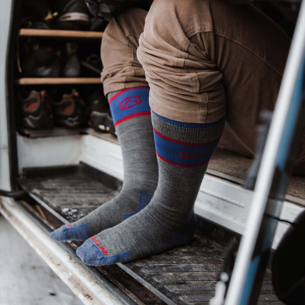 Man wearing Cloudline snowboard socks sitting in camper van with snowboard leaning next to him.