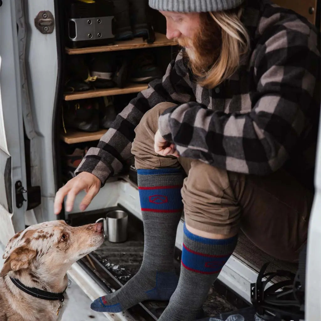 Man wearing Cloudline merino wool snowboard socks sitting in camper van petting dog.