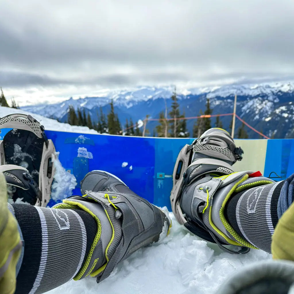 Snowboarder wearing Cloudline merino wool socks with one foot out sitting on snow.