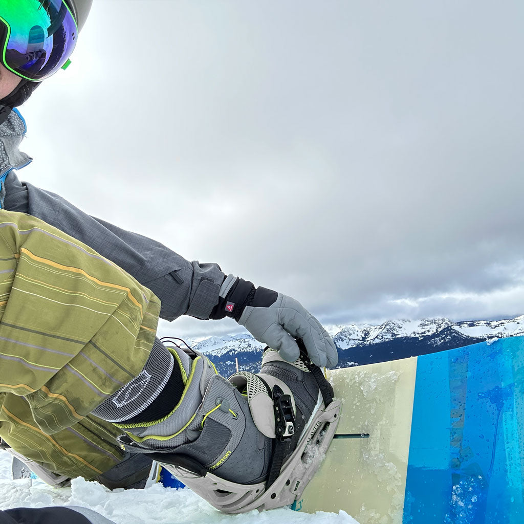 Snowboarder wearing Cloudline socks adjusting binding before a run.