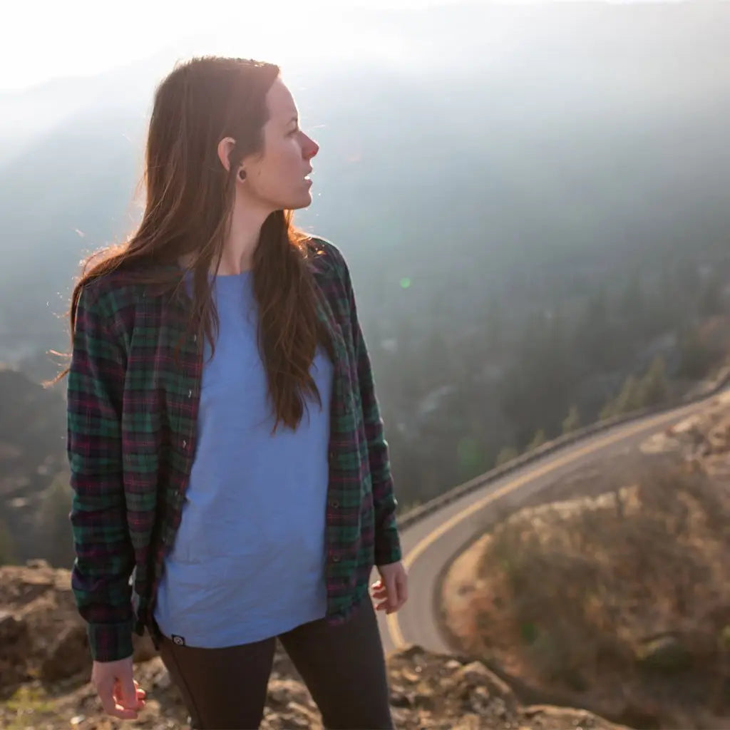 Women wearing Cloudline merino base layer standing on top of ridge with windy mountain road below.