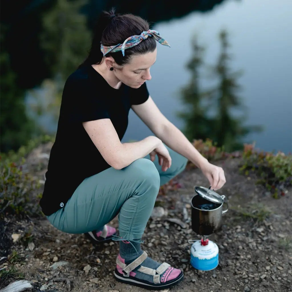 Backpacker wearing Cloudline merino tee crouched over backpacking stove boiling water.