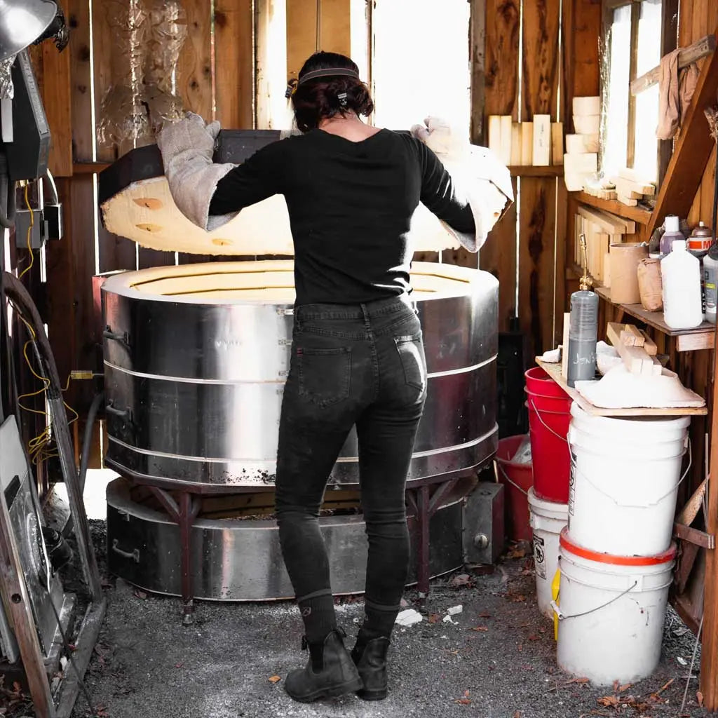 Women wearing Cloudline merino wool work socks lifting lid to kiln with back to camera.