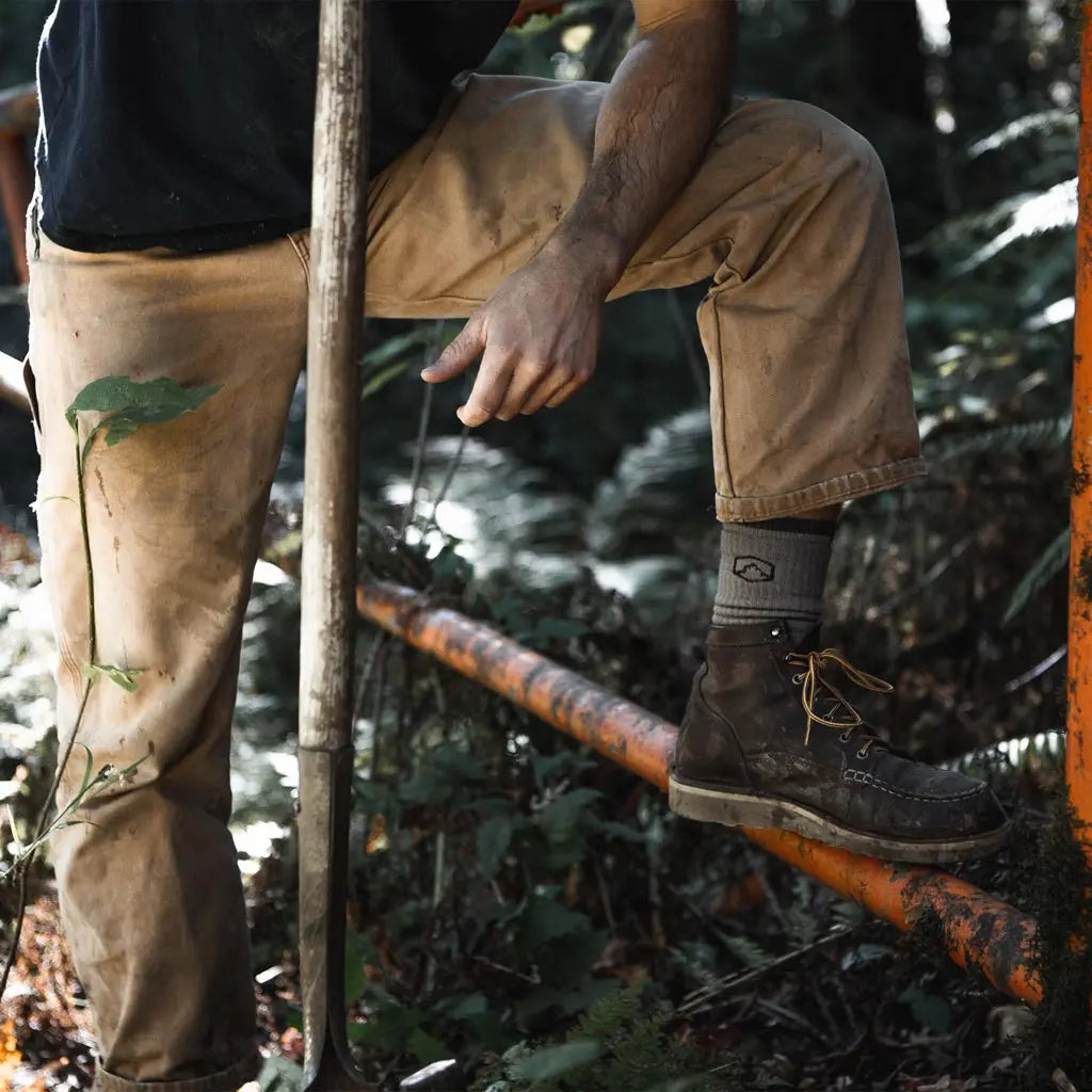 Man wearing Cloudline merino wool work socks resting foot on trailhead gate.