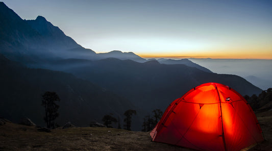 Illuminated camping tent in the backcountry with mountain sunset in the background at twilight.