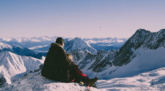 View from behind of couple snuggled up on a mountain top overlooking snowy mountain tops.