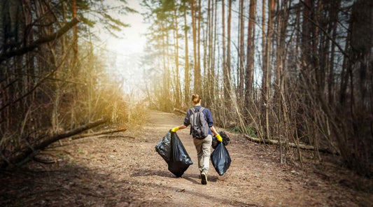 Hiker carrying out two large black trash bags from the woods.