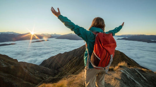 Backpacker holding up their arms while overlooking a lake and mountains at sunset.