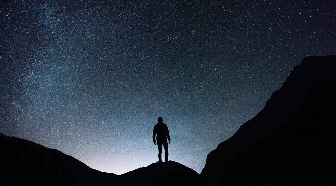 "Hiker's Silhouette on mountain boulder, gazing at the night sky.