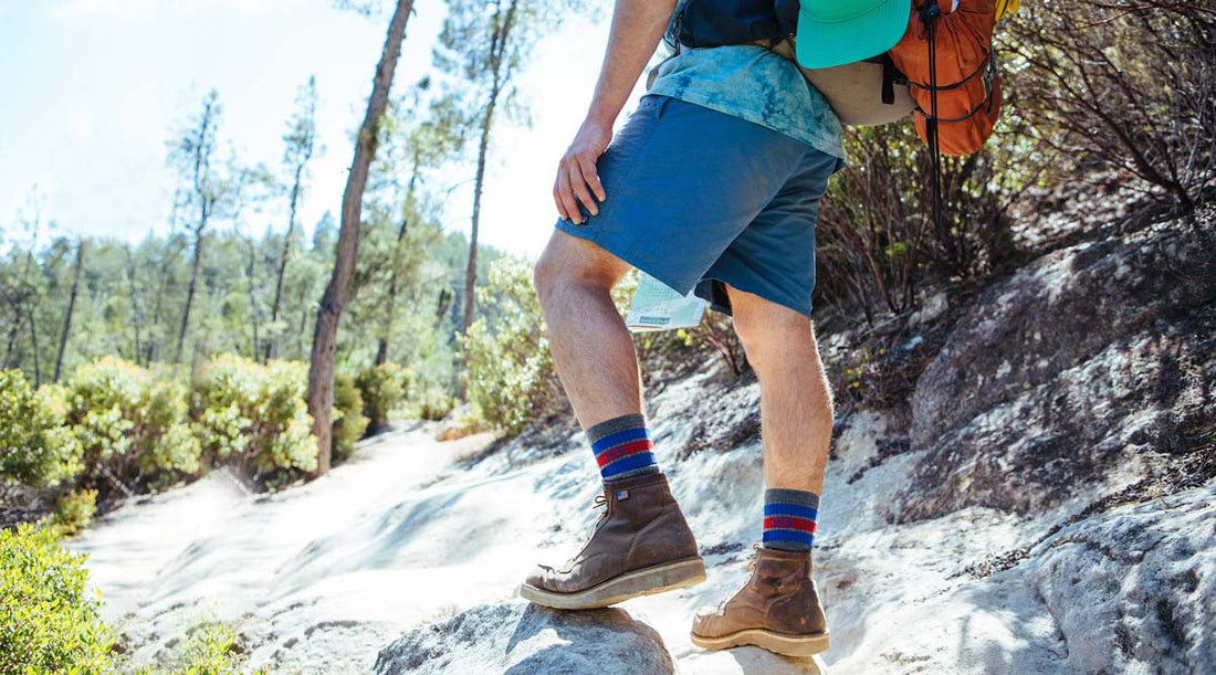 Hiker wearing Cloudline Apparel socks is hiking along a rocky trail on a sunny day.