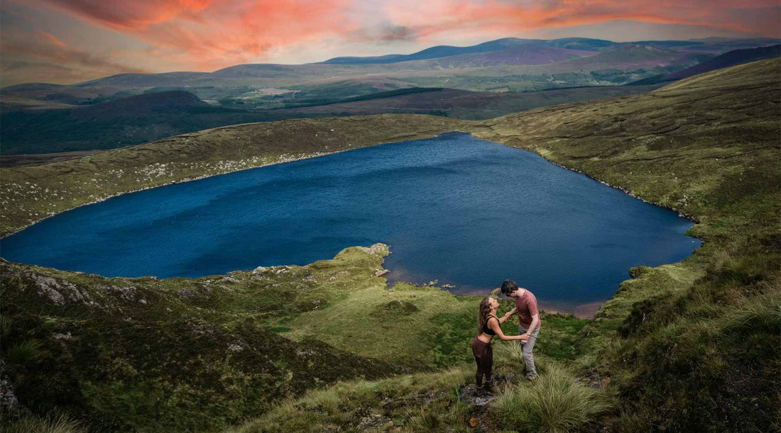 Couple holding hands above a heart shaped lake at sunset.