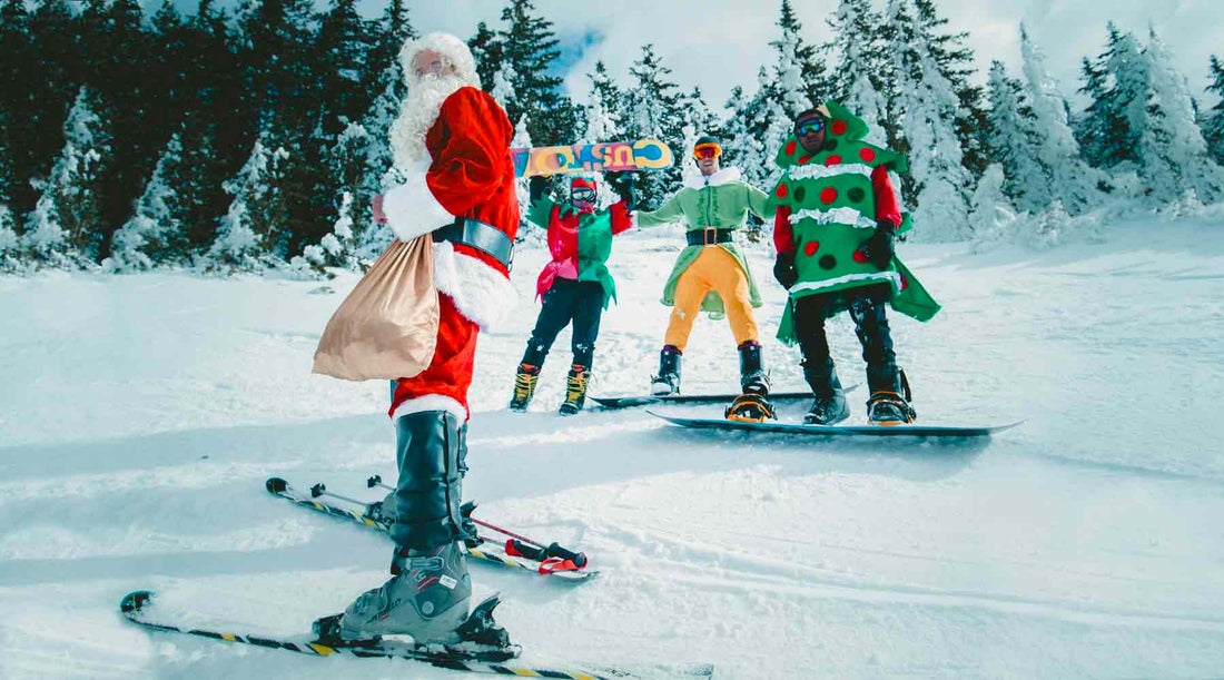 Skiers and snowboarders on ski slope dressed as santa and his elves and a christmas tree while they ski.