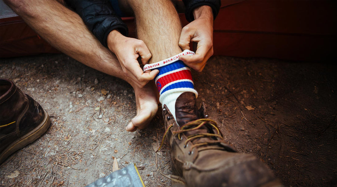 Backpacker sitting in open tent door putting on Cloudline moisture wicking merino wool hiking socks. 