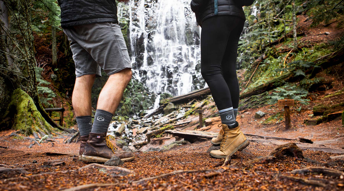 Two hikers wearing merino wool hiking socks and leather boots on a trail in front of a waterfall