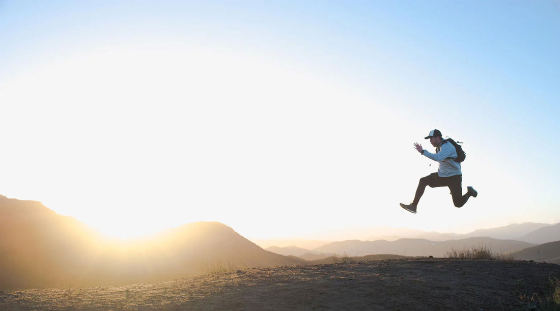 Adventurous hiker in mid-air, skipping along trail with sunset views.