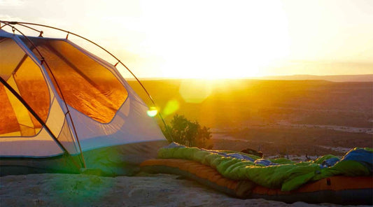 Sleeping bag on top of inflatable sleeping pad outside of tent at sunset.