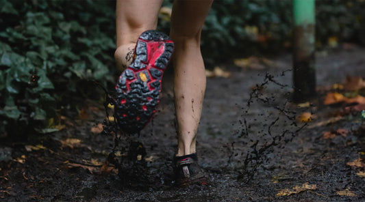 Trail runner running up muddy trail splashing through mud.