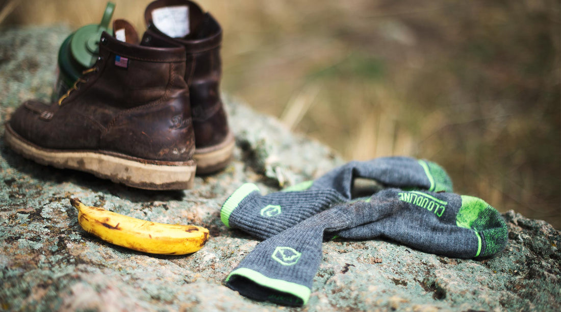 Merino wool hiking socks drying in the sun on a warm rock next to boots.