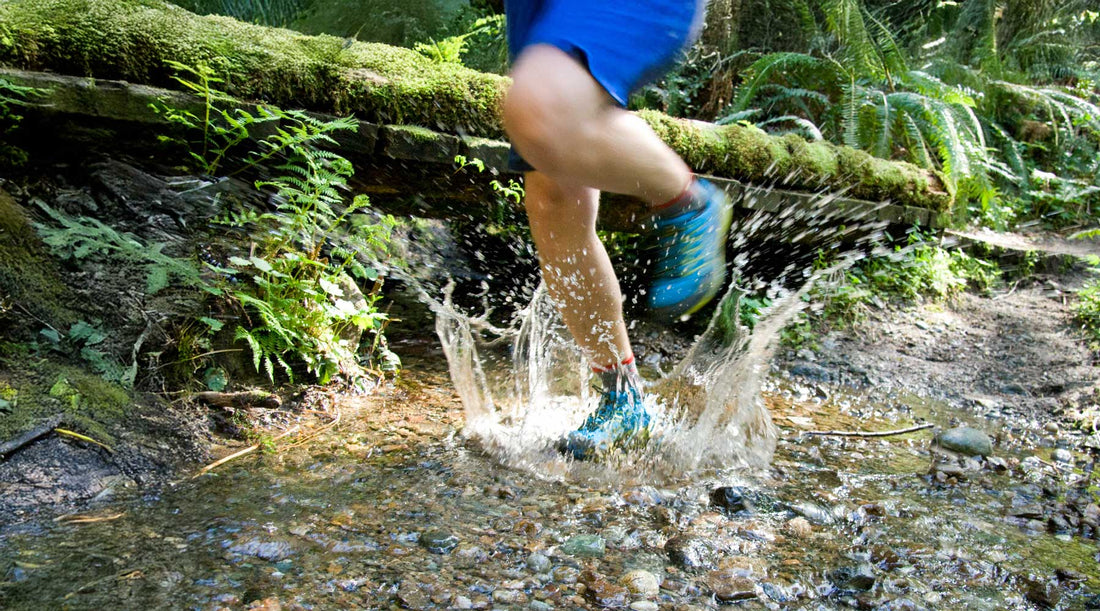 Man on a hiking trail, crossing a stream while wearing moisture wicking merino wool socks for hiking