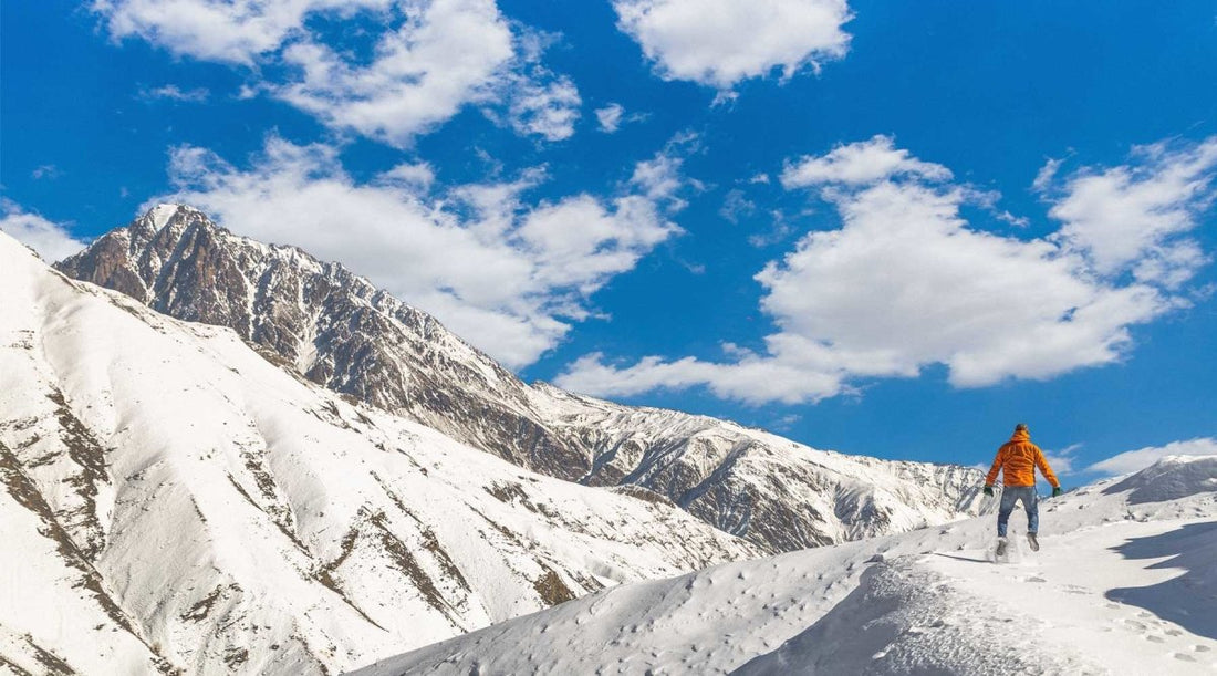 Hiker standing on snowy slope looking up at mountains above.