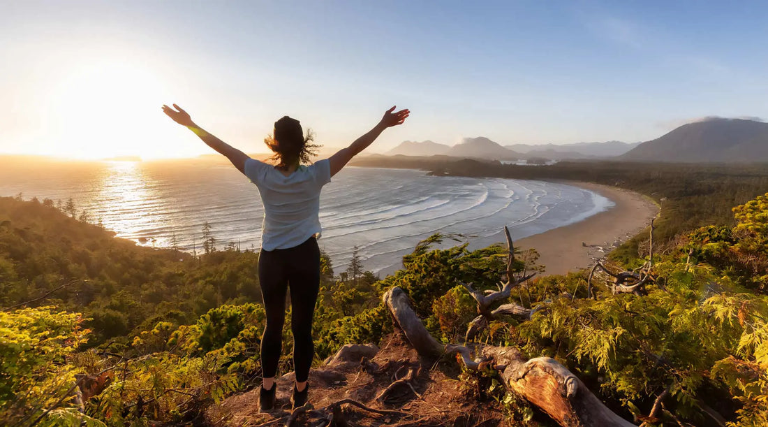 Hiker with raised arms enjoying a view of the ocean from hiking trail.