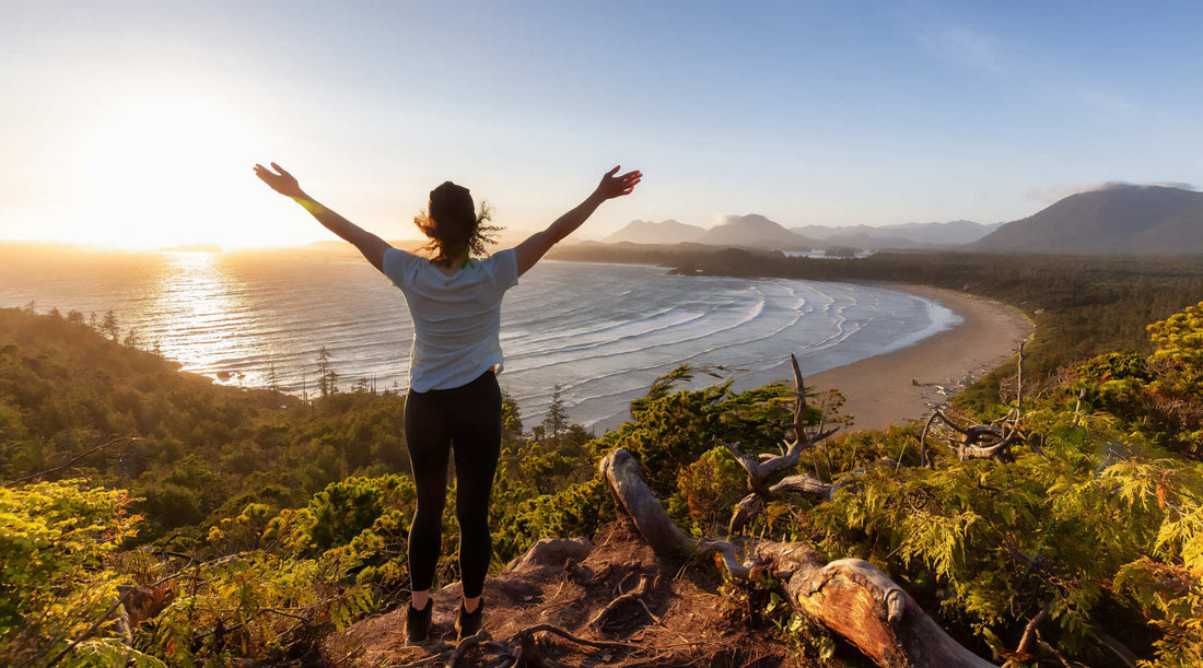 Hiker with raised arms enjoying a view of the ocean from hiking trail.