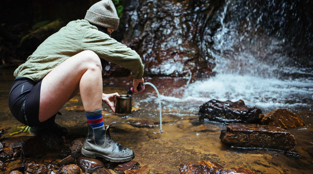 Women using a backpacking water filter to purify water from a stream.