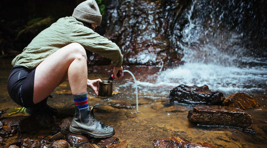 Women using a backpacking water filter to purify water from a stream.