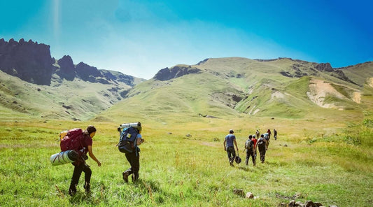 Large group of backpackers walking along grassy hills. 
