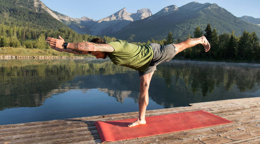 Man doin yoga on a dock next to a mountain lake.