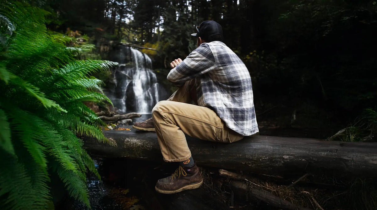 Hiker wearing Cloudline hiking socks and a hat sitting by a waterfall.