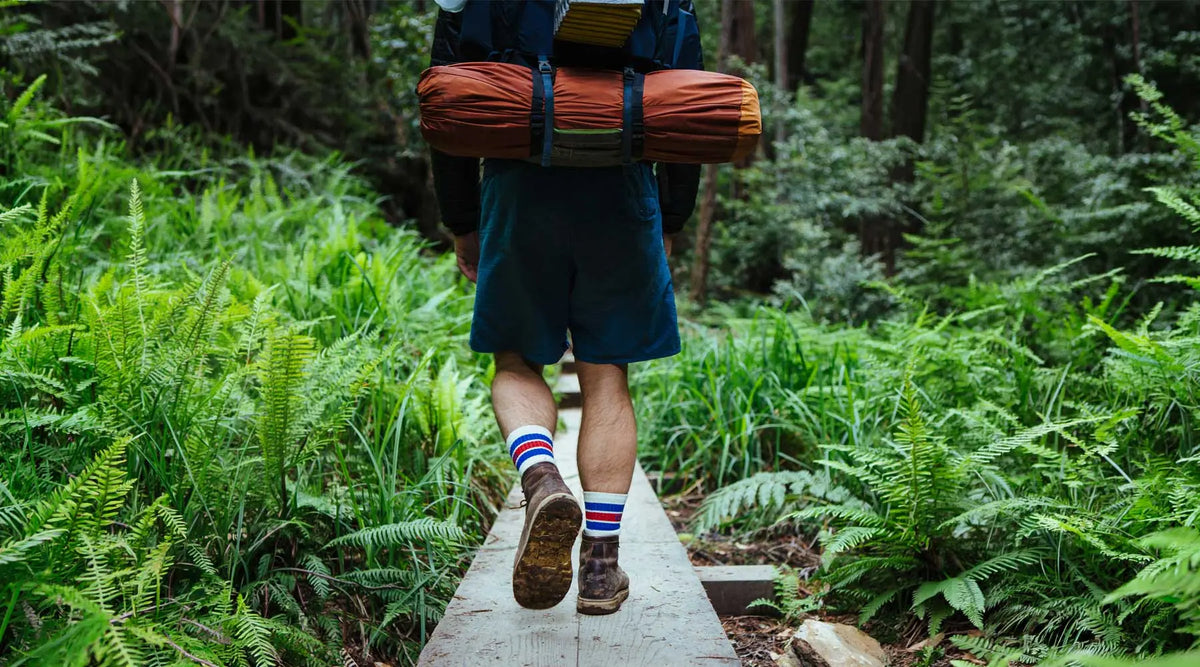 Backpacker wearing Cloudline merino wool socks while hiking over a trail bridge.