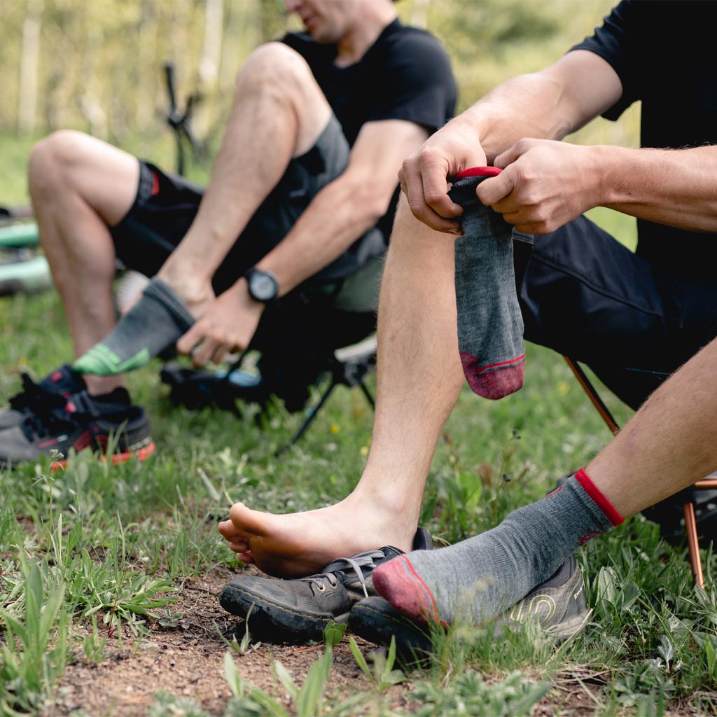 Two guys sitting in camp chairs putting on cloudline 1/4 top socks. 