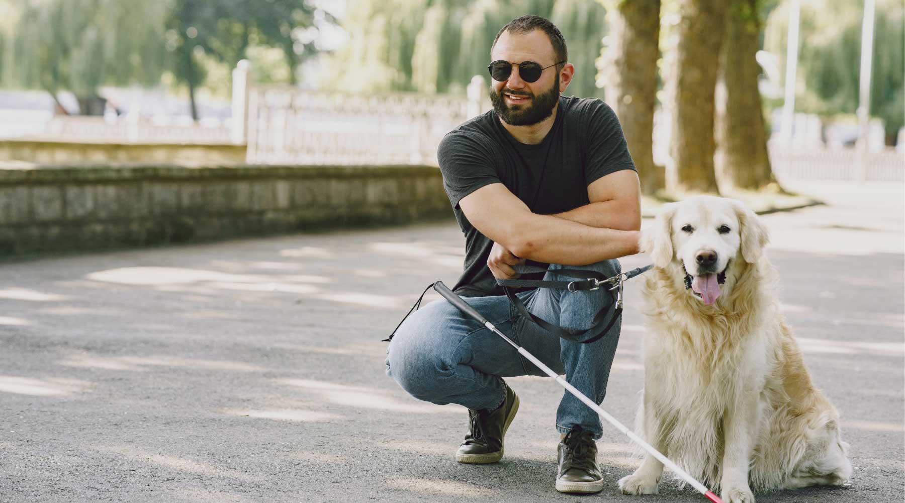 Blind man with cane crouching next to guide dog