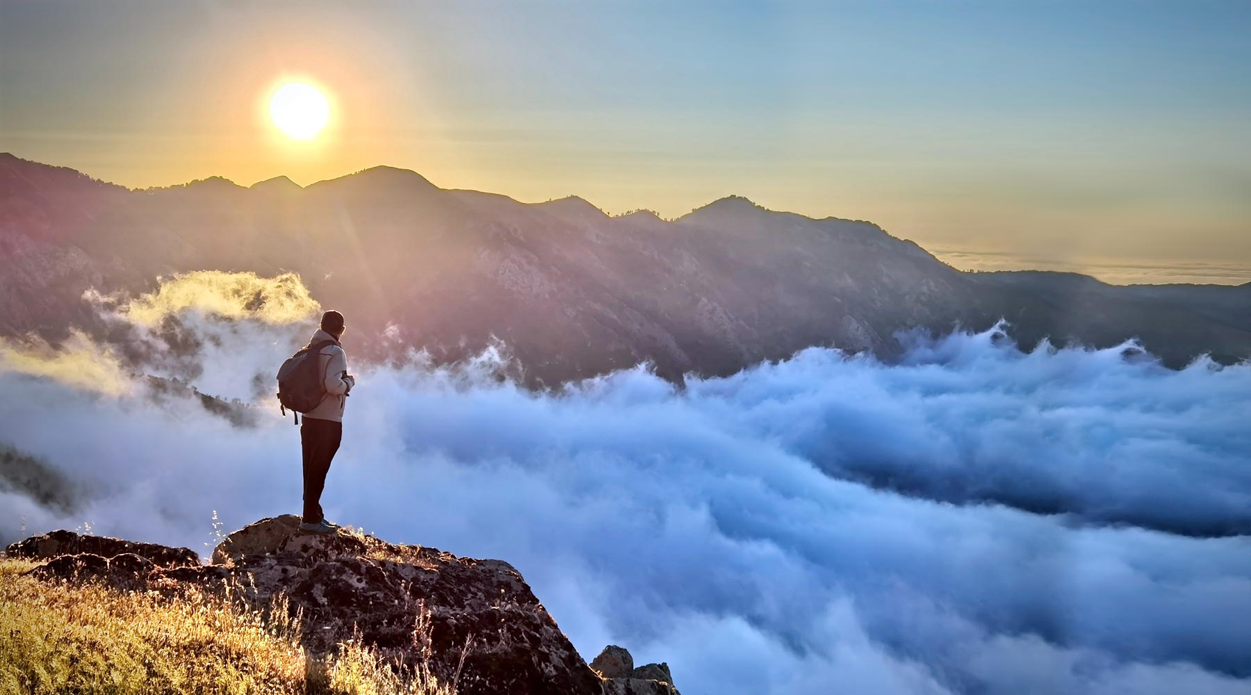 Hiker standing on mountain top above the clouds. 