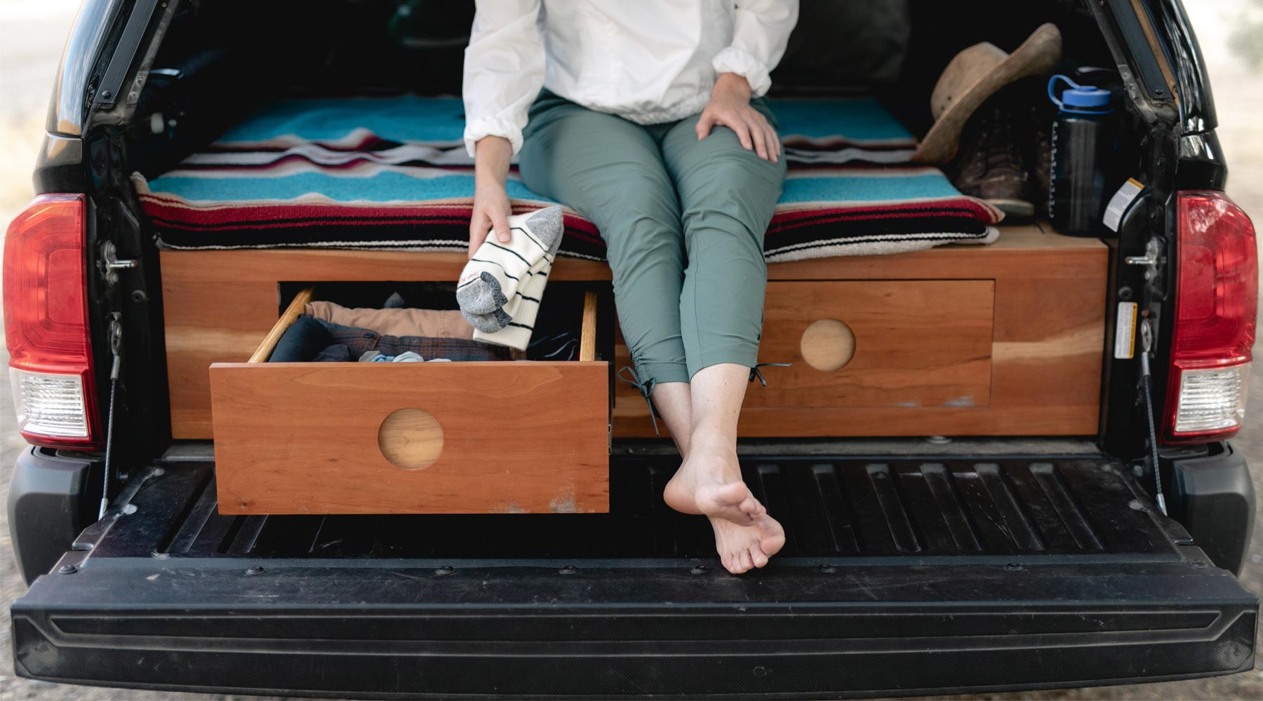 Camper sitting in back of converted truck camper putting Cloudline socks into under bed drawer.