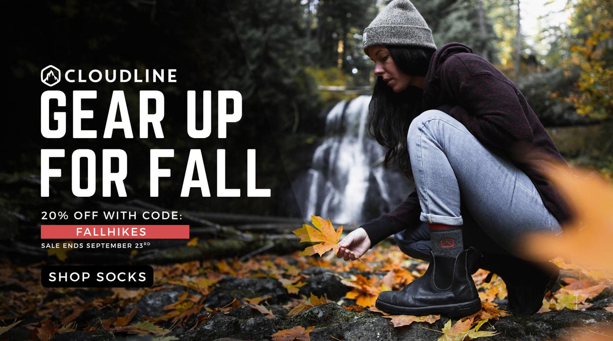 A promotional outdoor ad for Cloudline fall footwear and socks, showing a woman crouching in a forest near a waterfall while picking autumn leaves. Large text on the left reads 'CLOUDLINE GEAR UP FOR FALL' with sale details and 'SHOP SOCKS'.