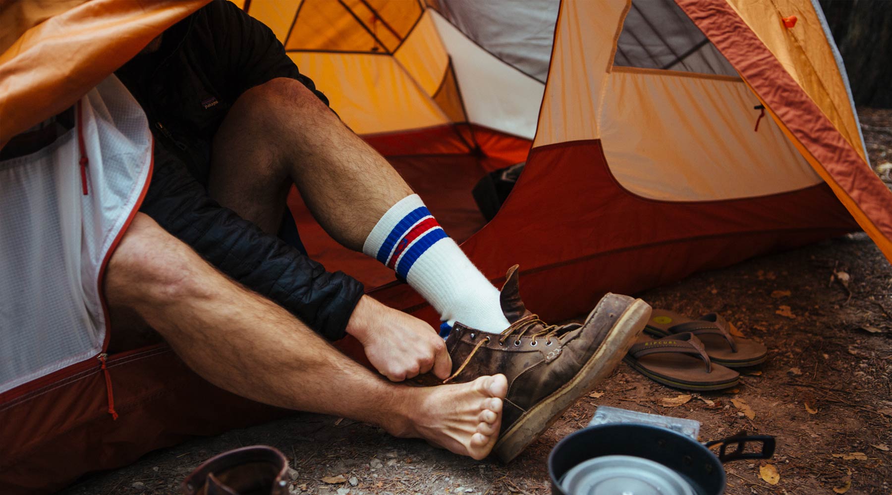 Backpacker sitting in tent putting on Cloudline socks and hiking boots. 