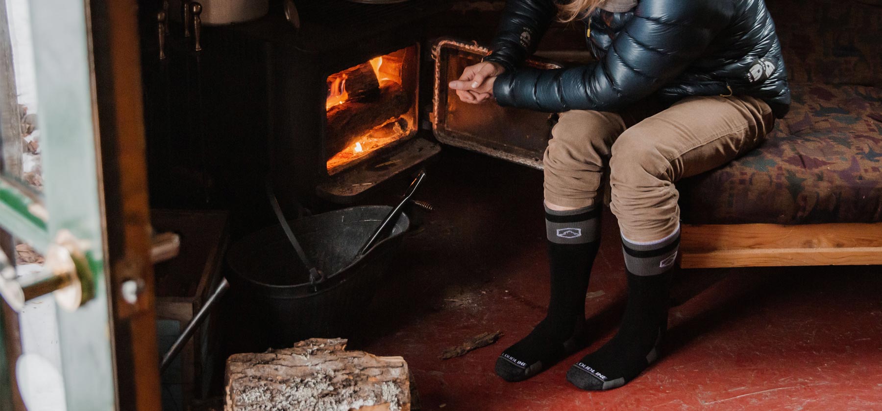 Man wearing Cloudline snow socks warming hands by the fire inside cabin. 