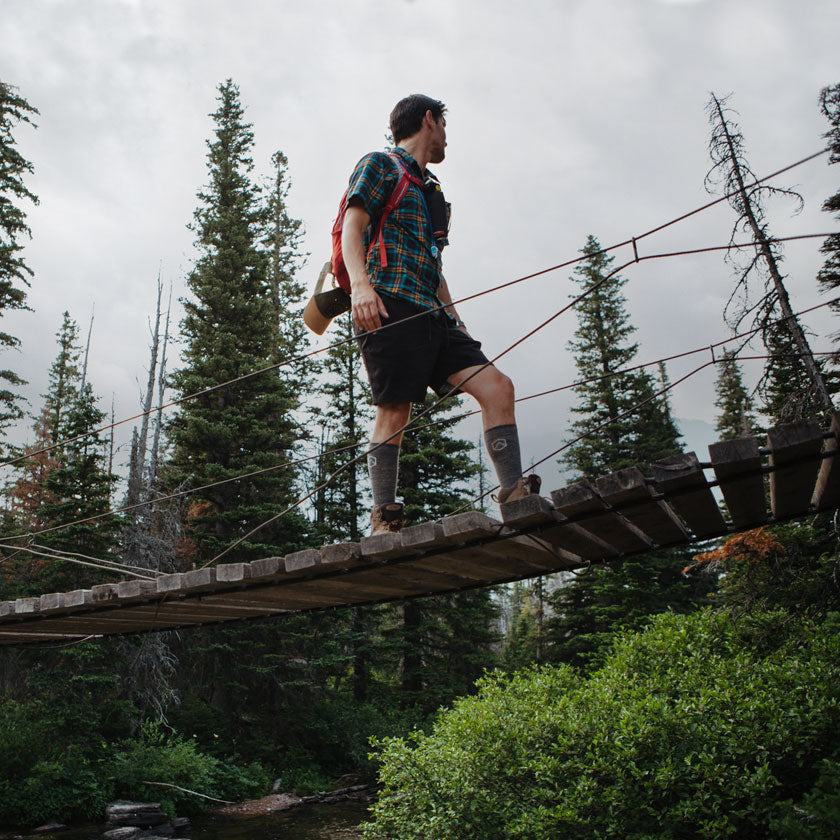 Man wearing Cloudline compression socks crossing a wooden trail bridge over stream. 