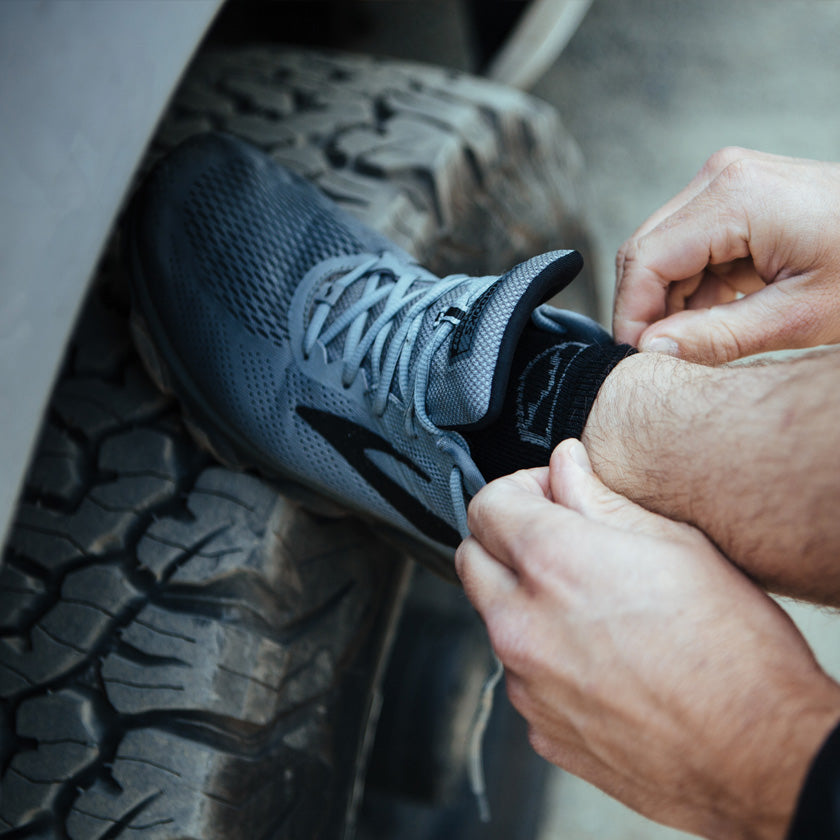 Man wearing Cloudline socks with foot up on camper van tire to tie running shoes. 