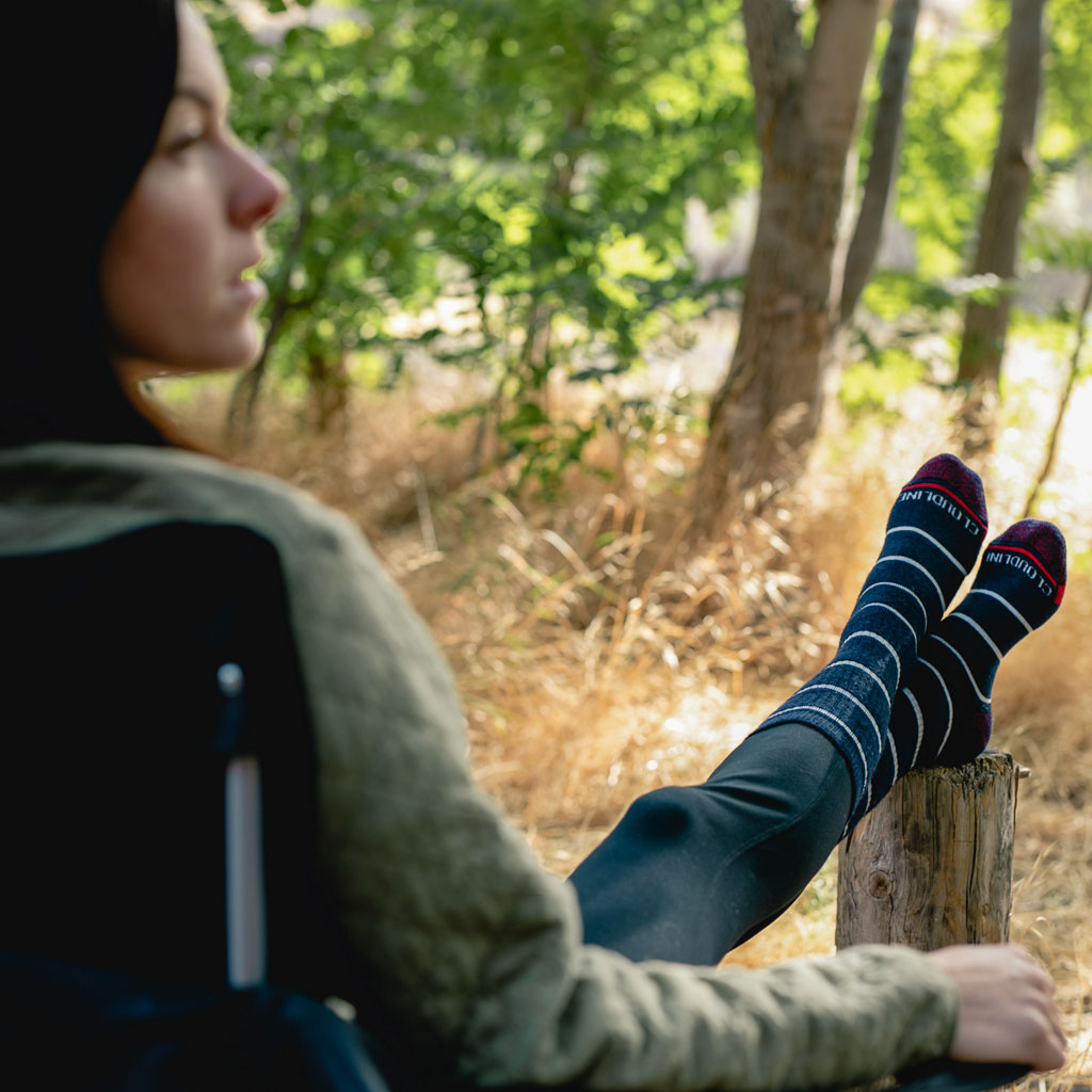 Women wearing Cloudline socks sitting in camp chair with feet up on log. 