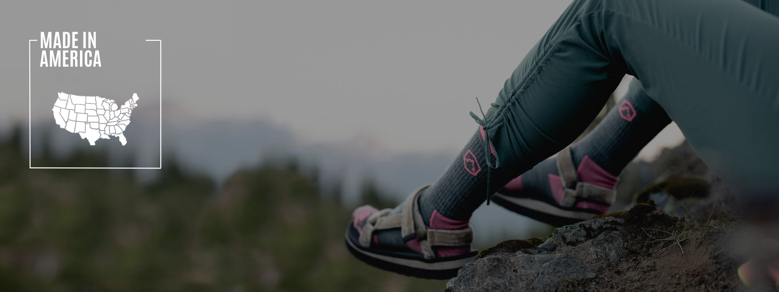 Hiker wearing Cloudline socks sitting on rock with mountain sunset in the background.