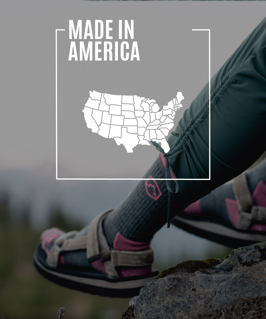 Hiker wearing Cloudline socks sitting on rock with mountain sunset in the background.