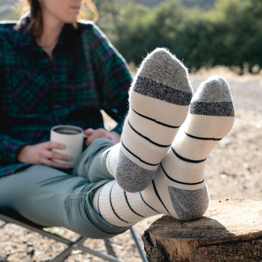 Women wearing Cloudline socks with feet up on log while having camp coffee