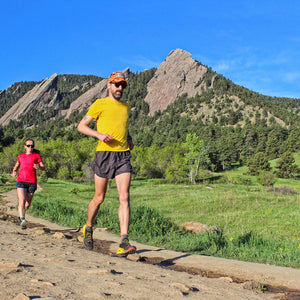 2 Trail runners running down trail with mountain towering in the distance. 