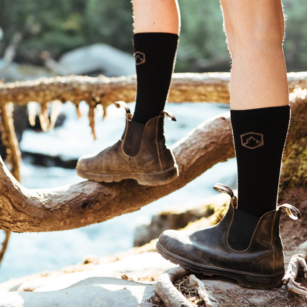 Hiker wearing Cloudline compression socks with fashionable boots, standing next to river. 