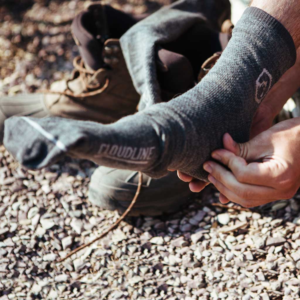 Man sitting next to trail putting on Cloudline compression socks. 