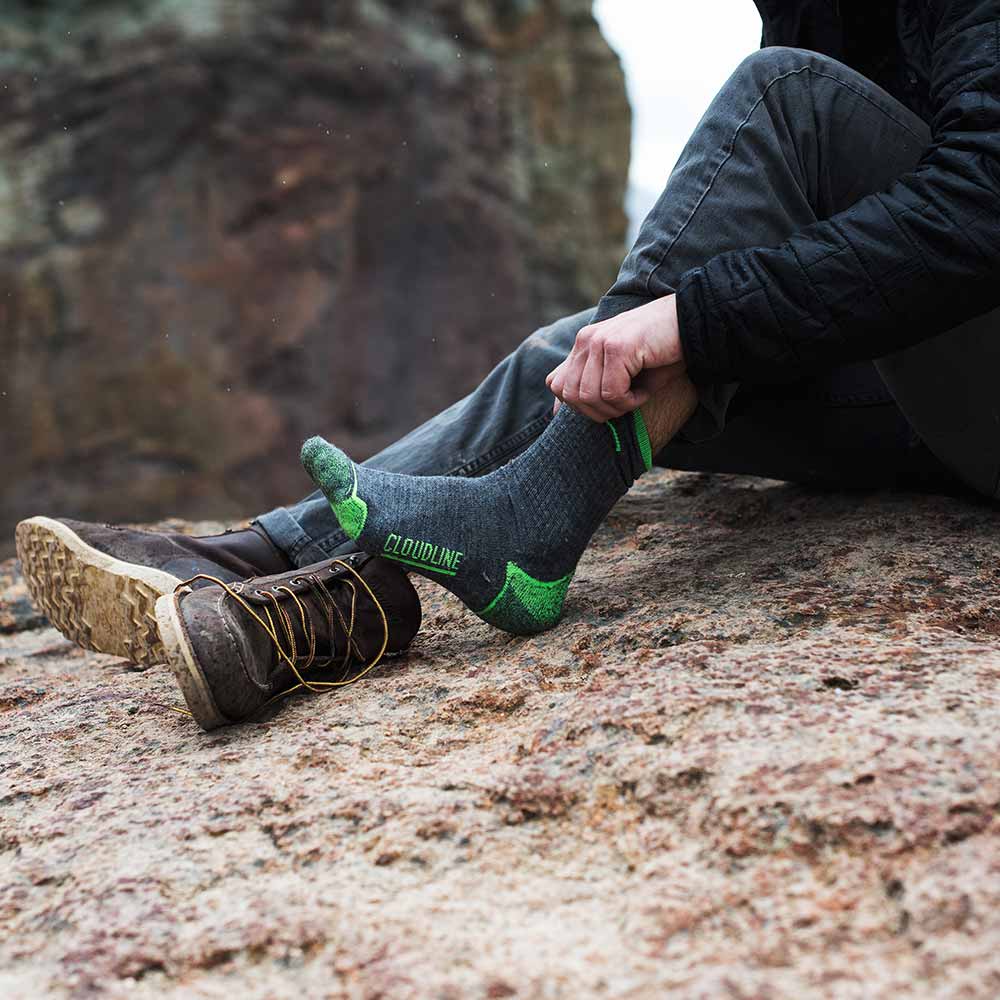 Hiker sitting on large rock pulling on Cloudline hiking socks.